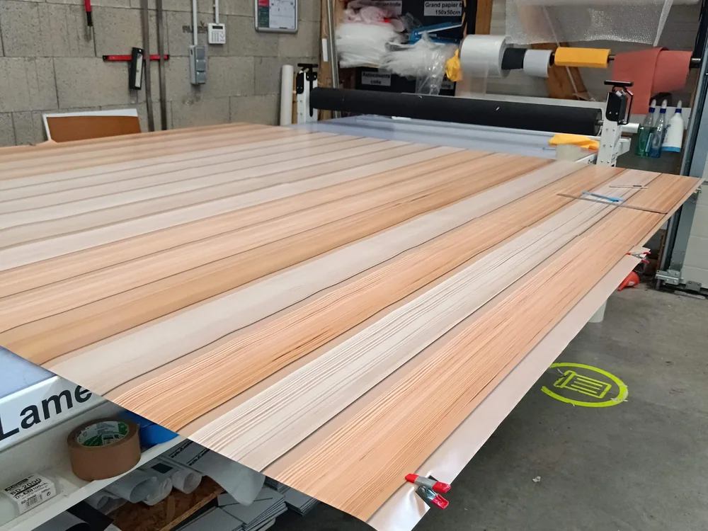 Lés imprimés effet bois en cours de sur-lamination sur la table de l'atelier ModulSkin, au Havre